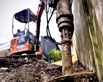 Excavator auger attachment drilling a precise post hole for structural foundations and footings.