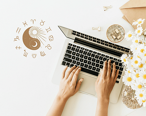 a woman typing in a bright area with chamomile flowers stationery and a graphic of a yin and yang moon and sun and an astrology wheel