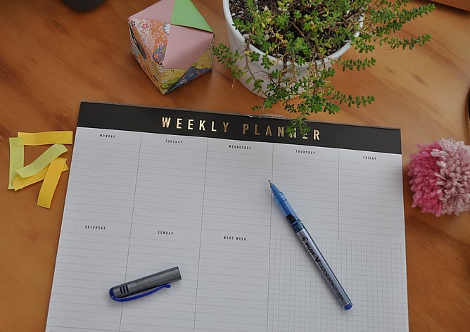 A weekly planner pad on a desk with pen at the ready