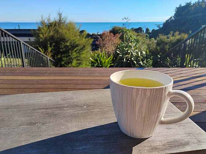 A cup of green tea on a table, with a view of the sea in the background