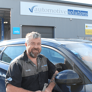 Automotive Solutions Kauri mechanic standing with a car he has completed a warrant on, in front of the building smiling