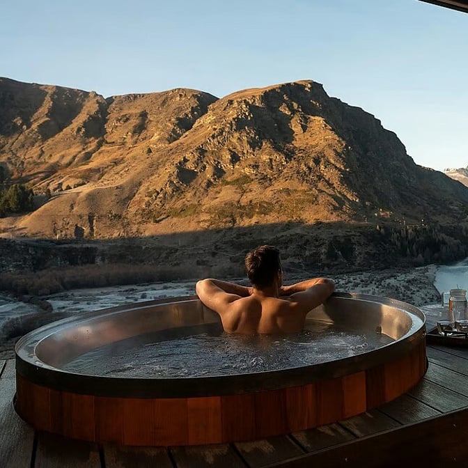 Couple relaxing in private outdoor hot tubs overlooking the Southern Alps and river, Queenstown high country