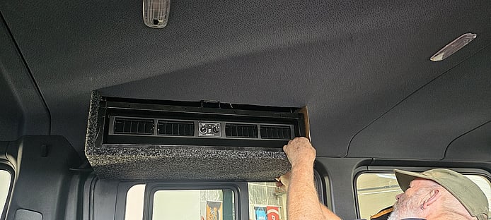 CoolCar technician fixing flush carpet to housing of rear air-conditioning roof-top unit in Mobility van