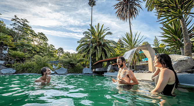 Visitors relaxing under thermal waterfalls in the outdoor hot pools at Taupo DeBretts