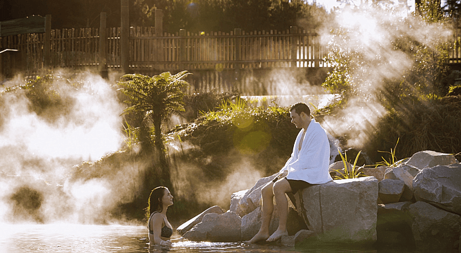 Geothermal steam rising around visitors soaking in free natural rock pools in Taupo