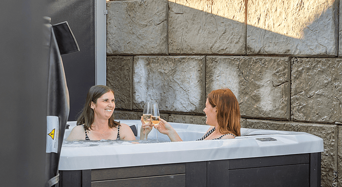 Two women relaxing in a private outdoor spa pool at Roam Taupo accommodation with champagne
