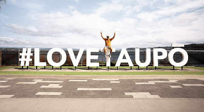 Man sitting on the iconic white Love Taupo sign along the Lake Taupo lakefront pathway