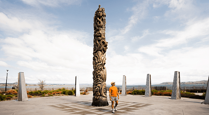 Man standing next to a tall Maori carved pou along the Lake Taupo waterfront walkway