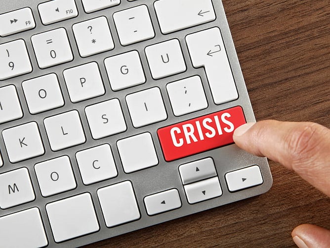 A keyboard on a desk has a red button labelled CRISIS, a finger is tapping the red buttonhe key