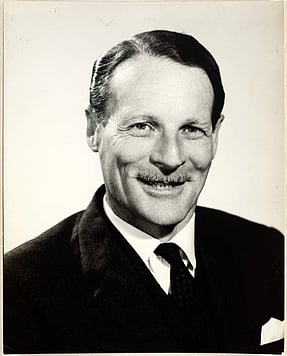 A man in suit and tie smiling at the camera. Black and white photo.