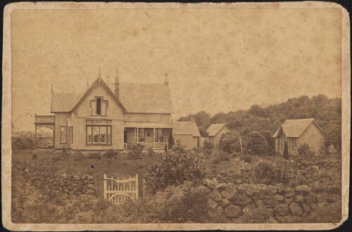 Sepia coloured photo of a house from the 1860s, land and a stone wall.