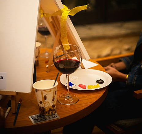 Person sitting at a table with paints, canvases and a glass of wine. Paula Charlton's Paint & Sip workshop for Waimarino Arts Awards 2026. Image by Photo by <a href="https://unsplash.com/@chriscreations__?utm_source=unsplash&utm_medium=referral&utm_content=creditCopyText">Christian Agbede</a> on <a href="https://unsplash.com/photos/a-glass-of-wine-sitting-on-top-of-a-wooden-table-Fbjs3BFfruU?utm_source=unsplash&utm_medium=referral&utm_content=creditCopyText">Unsplash</a>