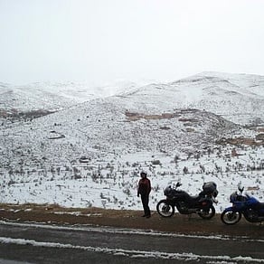 Two touring motorcycles beside a snow-covered mountain landscape in Morocco