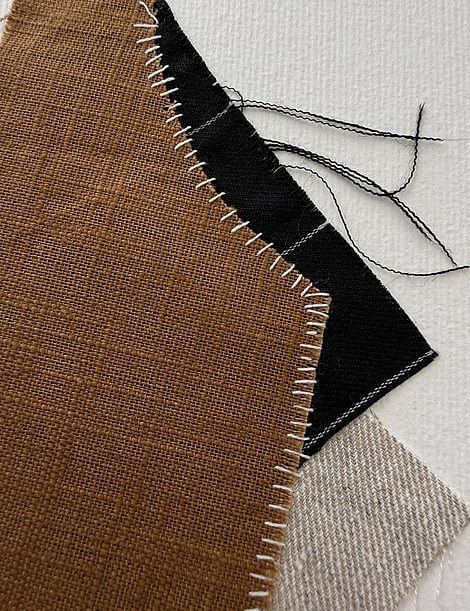detail image of earth-toned linen and cotton fragments, showing weave texture and soft frayed edges and white hand-stitched details