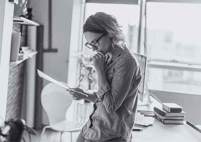 Woman standing in an office reading a document thoughtfully before signing