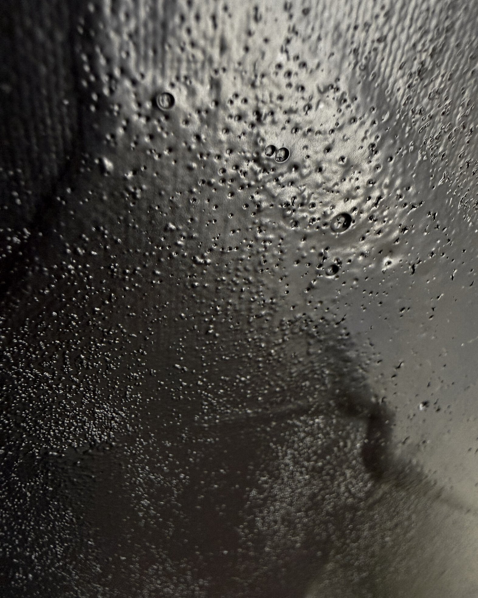 detail image of warm black acrylic and silica sand surface, showing glossy pooled paint with dense pitting, granular texture and variations in sheen revealed by directional light 