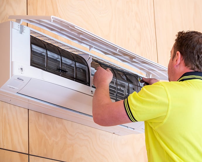 Technician cleaning the filters of a wall-mounted heat pump during a service