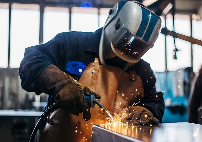 Tradesperson welding with sparks, wearing full safety gear