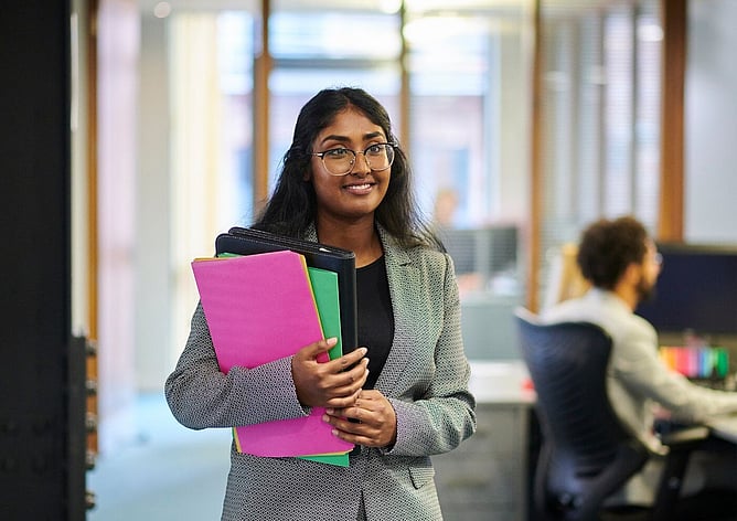 Young professional woman holding folders in an office hallway