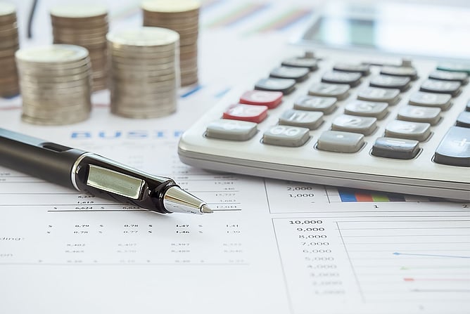 Calculator, pen and stacked coins on financial documents with dollar figures