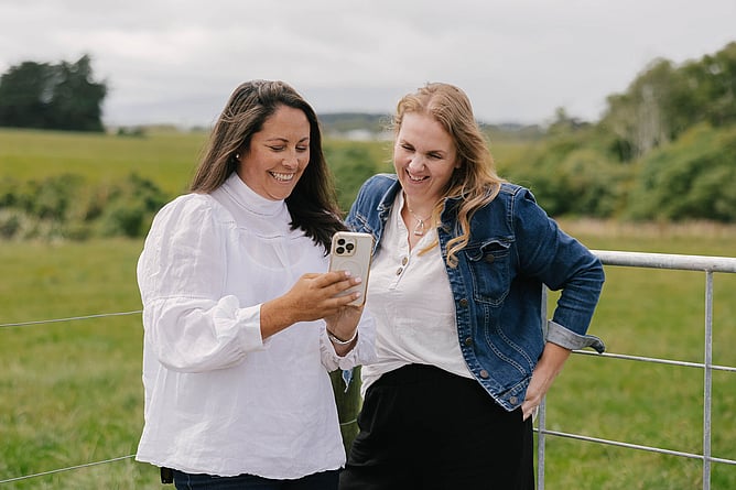 Amber and Cheyenne look at a phone together in a field
