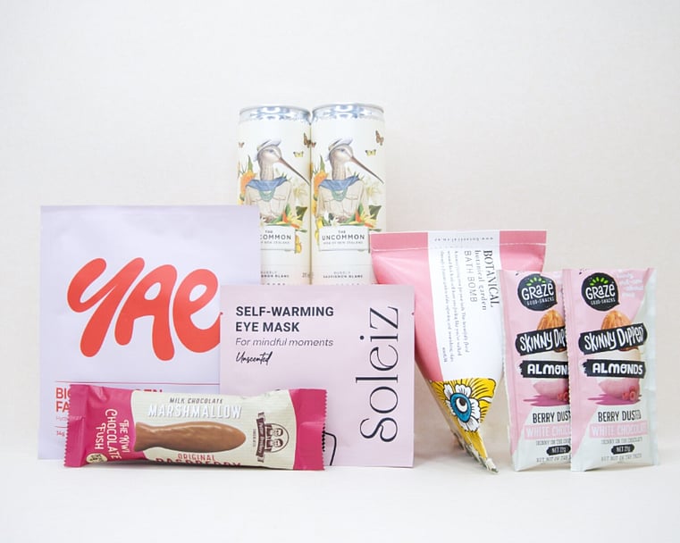 A Little Pick Me Up Gift Box featuring Uncommon sparkling wine, Soleiz eye mask, YAE face mask, Botanicals bath bomb, chocolate fish, and gourmet nuts, beautifully packaged as a self-care gift box under $100.