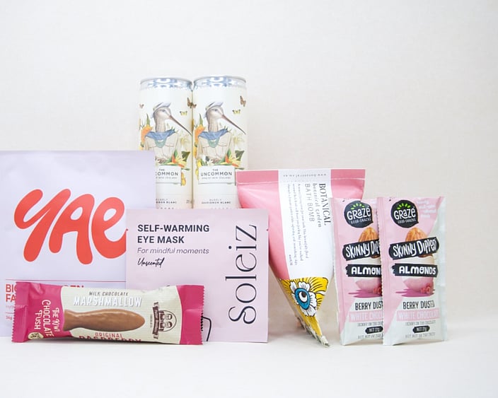 A Little Pick Me Up Gift Box featuring Uncommon sparkling wine, Soleiz eye mask, YAE face mask, Botanicals bath bomb, chocolate fish, and gourmet nuts, beautifully packaged as a self-care gift box under $100.
