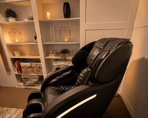 Picture of a massage chair in a treatment room with candles flickering in the background in the shelving unit