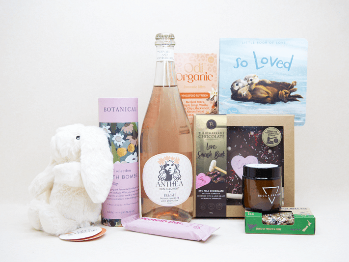 Celebrate The New Mum Gift Box featuring Anthea alcohol-free sparkling wine, Lily & George teddy bear, So Loved baby book, Becca Project candle, Botanicals bath bombs, artisan chocolate, and nourishing treats, beautifully packaged for new mums and new babies.