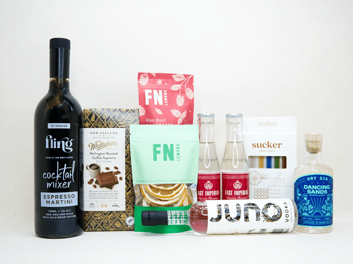 The Drinks Cart gift box featuring Juno Vodka, Dancing Sands Gin, Fling Margarita Mixer, East Imperial tonic water, FN citrus garnishes, raspberry sugar dust, Sucker glass straws, and Whittaker's coffee chocolate, beautifully packaged for cocktail lovers and entertaining.