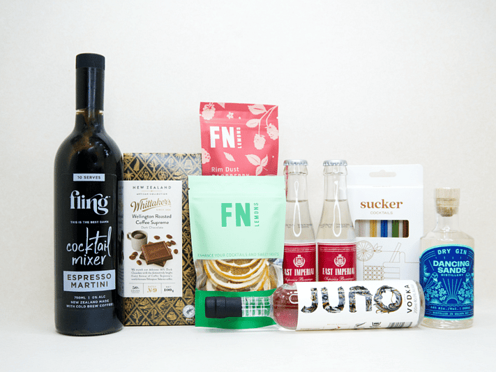 The Drinks Cart gift box featuring Juno Vodka, Dancing Sands Gin, Fling Margarita Mixer, East Imperial tonic water, FN citrus garnishes, raspberry sugar dust, Sucker glass straws, and Whittaker's coffee chocolate, beautifully packaged for cocktail lovers and entertaining.
