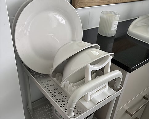 Picture of a small trolle next to the bathroom vanity. it has a small drying rack that has dishes on that have been washed.