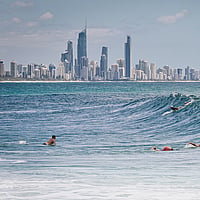 Surfers and swimmers ducking through a wave with skyline in the background