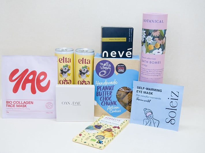 Care Package Gift Box featuring an OAN DAE wish paper kit, Soleiz eye masks, Nevé candle, floral bath bombs, Molly Woppy peanut butter cookies, YAE face mask, Bennetto chocolate, and Elta Ego self-care products, beautifully packaged to encourage relaxation and wellbeing