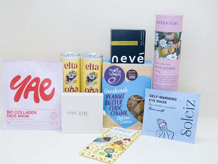 Care Package Gift Box featuring an OAN DAE wish paper kit, Soleiz eye masks, Nevé candle, floral bath bombs, Molly Woppy peanut butter cookies, YAE face mask, Bennetto chocolate, and Elta Ego self-care products, beautifully packaged to encourage relaxation and wellbeing