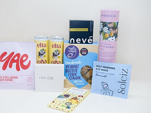 Care Package Gift Box featuring an OAN DAE wish paper kit, Soleiz eye masks, Nevé candle, floral bath bombs, Molly Woppy peanut butter cookies, YAE face mask, Bennetto chocolate, and Elta Ego self-care products, beautifully packaged to encourage relaxation and wellbeing