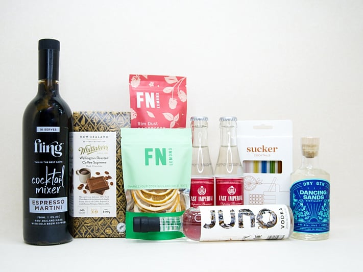 The Drinks Cart gift box featuring Juno Vodka, Dancing Sands Gin, Fling Margarita Mixer, East Imperial tonic water, FN citrus garnishes, raspberry sugar dust, Sucker glass straws, and Whittaker's coffee chocolate, beautifully packaged for cocktail lovers and entertaining.
