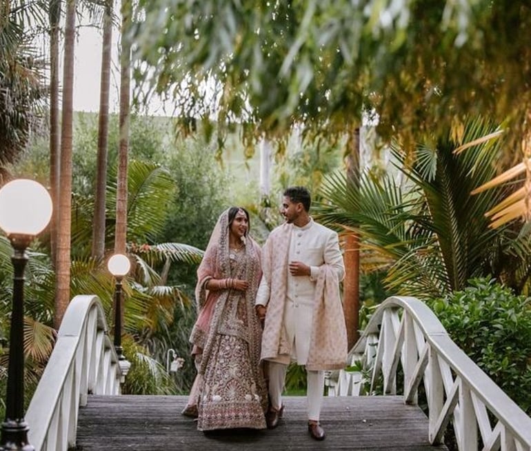 Indian wedding couple walking across a garden bridge at Settlers Country Manor Auckland