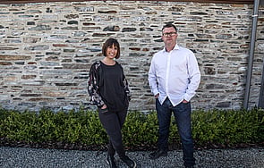 Sian Taylor and Mark Read of Team Green Architects standing in front of a stone building with decorative hedging