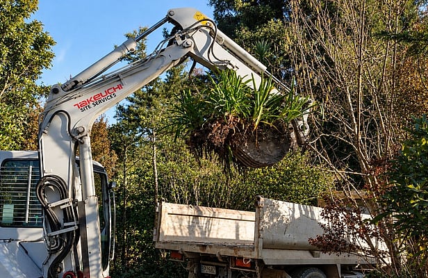 Digger removing established plants during a garden clear-out in Nelson