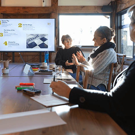 Mel Curwood facilitating a Cash-flow Reset workshop, talking with a business owner while her framework is on screen behind them.