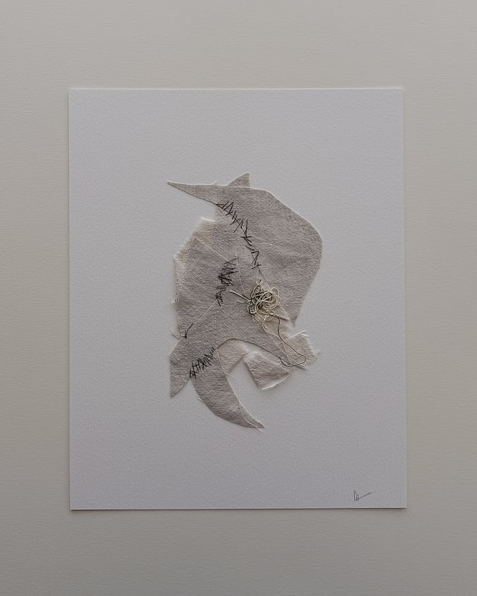 full image of a layered collage on soft white fabriano, showing repurposed oat and fawn-toned linen, with the oat-toned base twisted into a ribbon-like form and angular fawn-toned fragments layered on top, hand-stitched detail, visible weave texture, soft frayed edges and a messy swirl of thread remnants resting on one of the fragments, with hanging threads and handwritten signature in lower right corner 