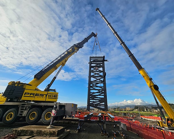 Two cranes position structural steel into place on site at Ngākōroa railway station