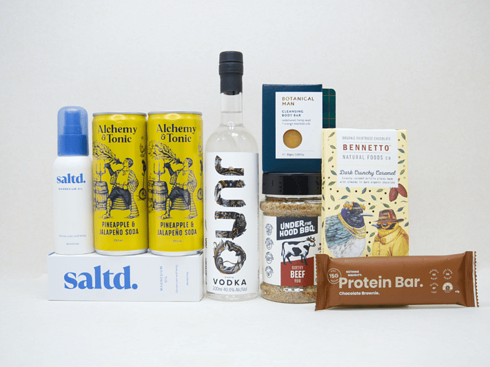 The Kick Back Gift Box featuring JUNO Vodka, Saltd Magnesium spray, Botanicals body bar, Bennetto chocolate, Under the Hood BBQ spice, Nothing Naughty protein bar and Alchemy tonic mixers.