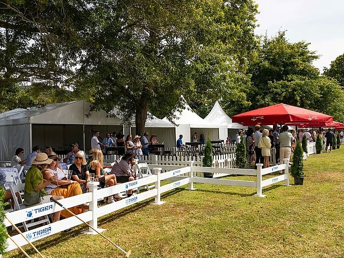 Outdoor gathering beside a white marquee with shaded seating and red umbrellas