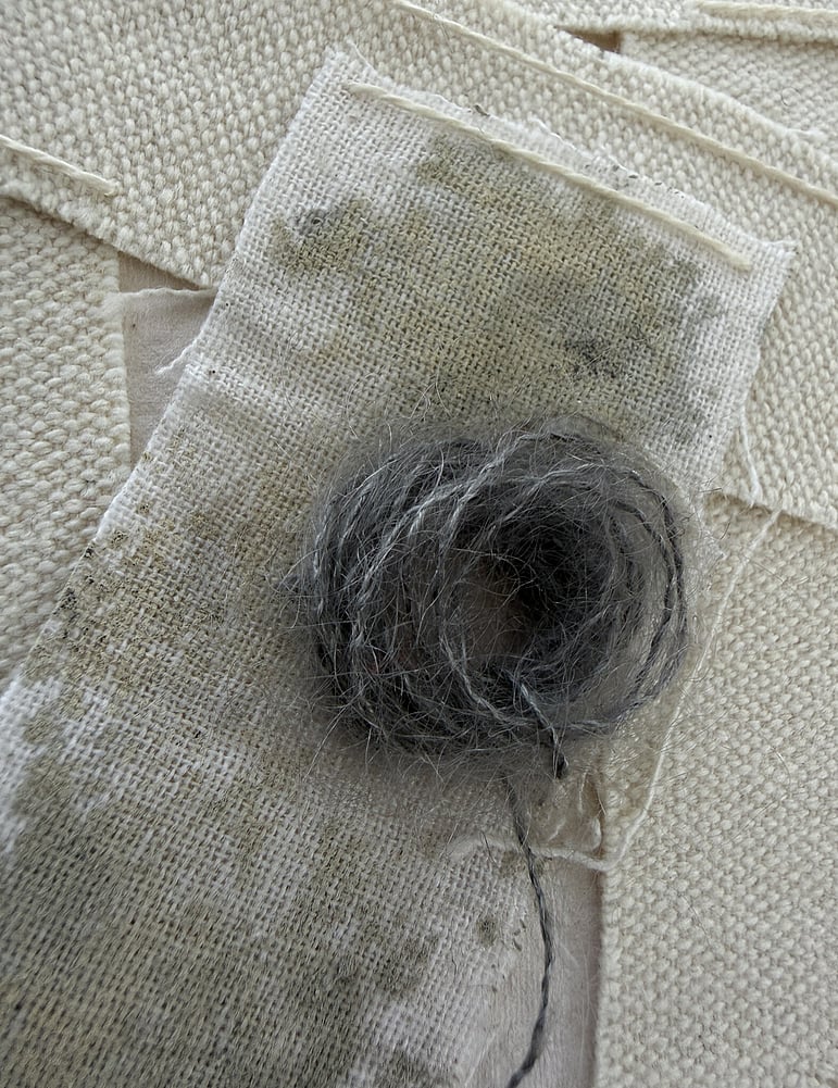 detail image of layered repurposed oat-toned linen and cotton fragments, one blotted with grey-green acrylic, varied weave textures, soft frayed edges and a swirl of charcoal baby alpaca/silk blend yarn remnant 