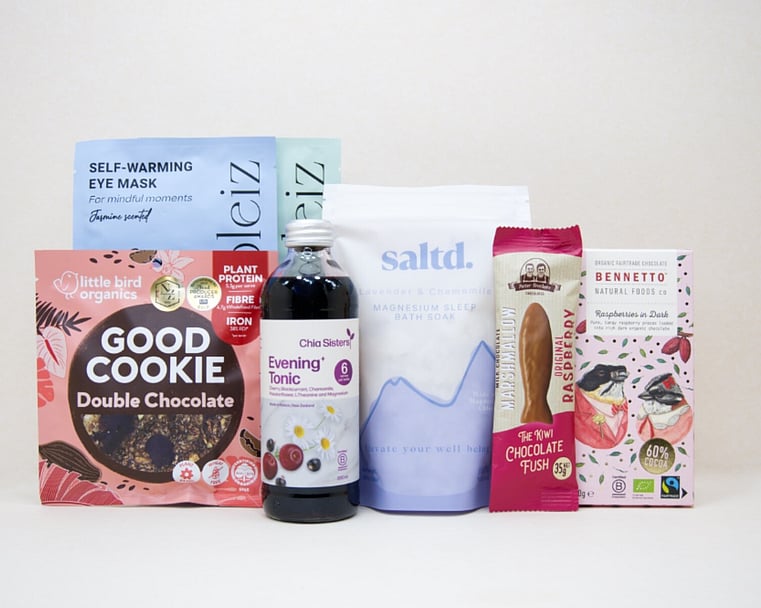 A Little Unwind Gift Box featuring Chia Sisters Evening Tonic, Saltd Magnesium Soak, Soleiz eye masks, Little Bird Organics Good Cookie, Bennetto raspberry chocolate, and Potter Brothers raspberry chocolate fish, thoughtfully curated for relaxation, rest, and self-care.