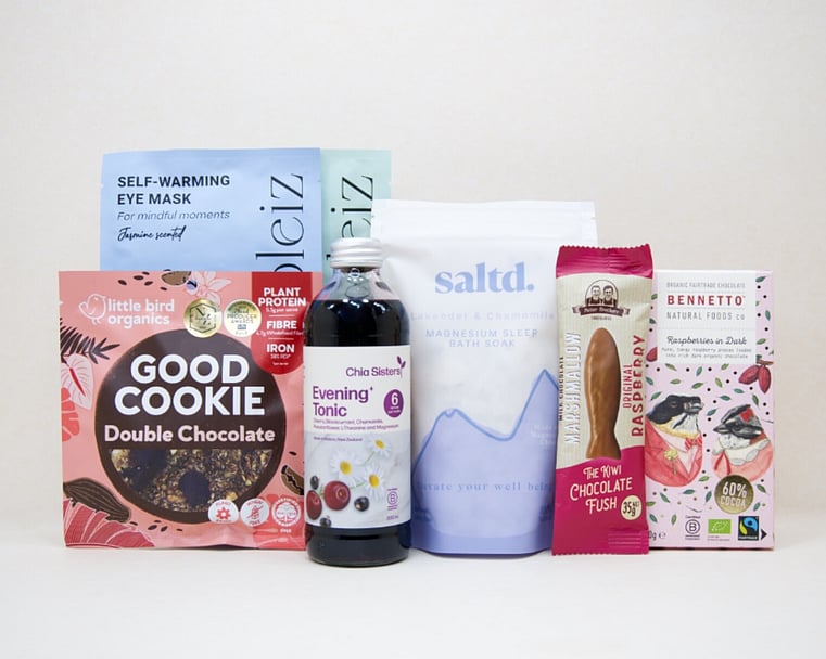 A Little Unwind Gift Box featuring Chia Sisters Evening Tonic, Saltd Magnesium Soak, Soleiz eye masks, Little Bird Organics Good Cookie, Bennetto raspberry chocolate, and Potter Brothers raspberry chocolate fish, thoughtfully curated for relaxation, rest, and self-care.