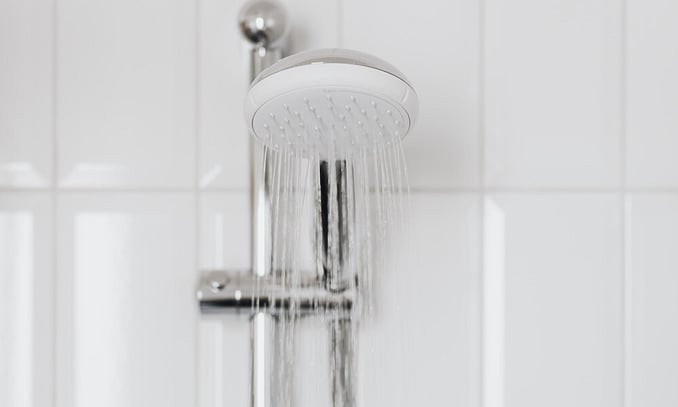 Water running from a modern chrome shower head mounted on an adjustable sliding bar against white bathroom tiles.