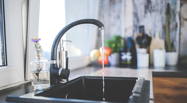A modern black gooseneck kitchen faucet with running water over a matching dark sink, placed next to a bright window.